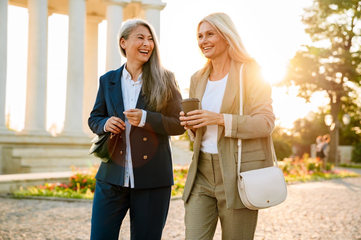 Mature multiracial businesswomen talking and drinking coffee during walking outdoors