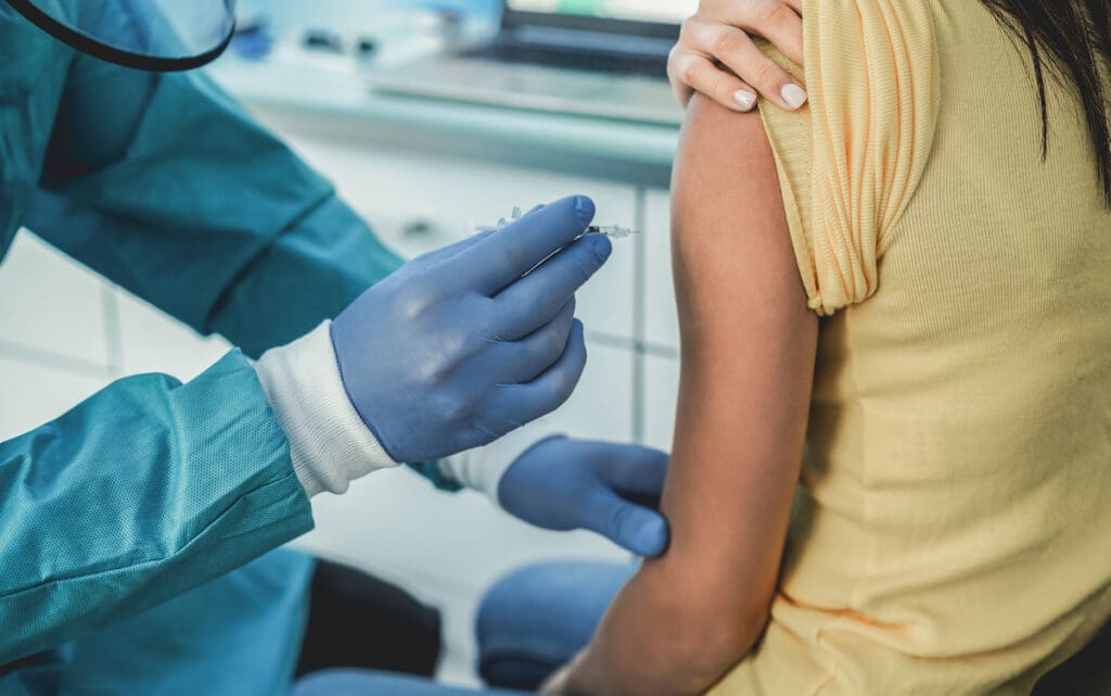 Doctor with hazmat suit and protective gloves giving patient a vaccine for coronavirus disease - Focus on woman hand